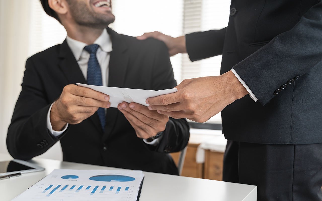 En smilende mann sitter og en mann står og sammen holder deg på et kort. Foto