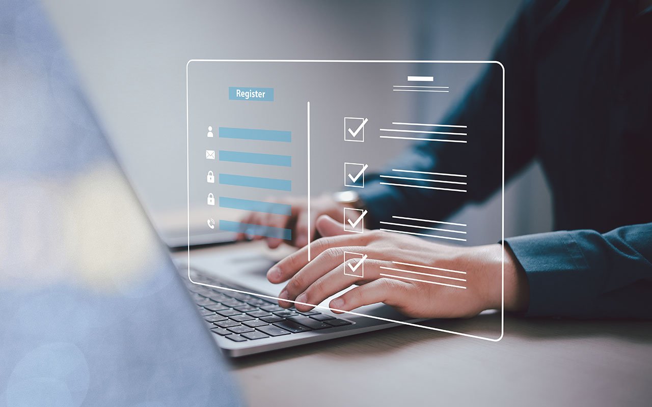 Hender som skriver på laptop med digitalt registreringsskjema og avkrysningsbokser i forgrunnen.