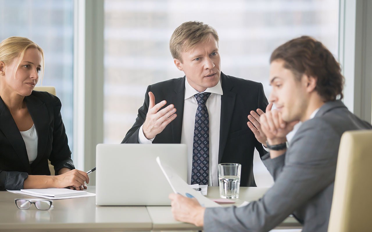 En kvinne og to menn sitter rundt et bord og prater