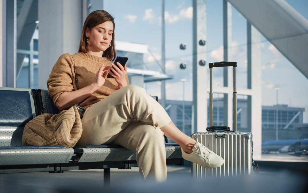 En kvinne sitter på en flyplass med en mobil i hånden