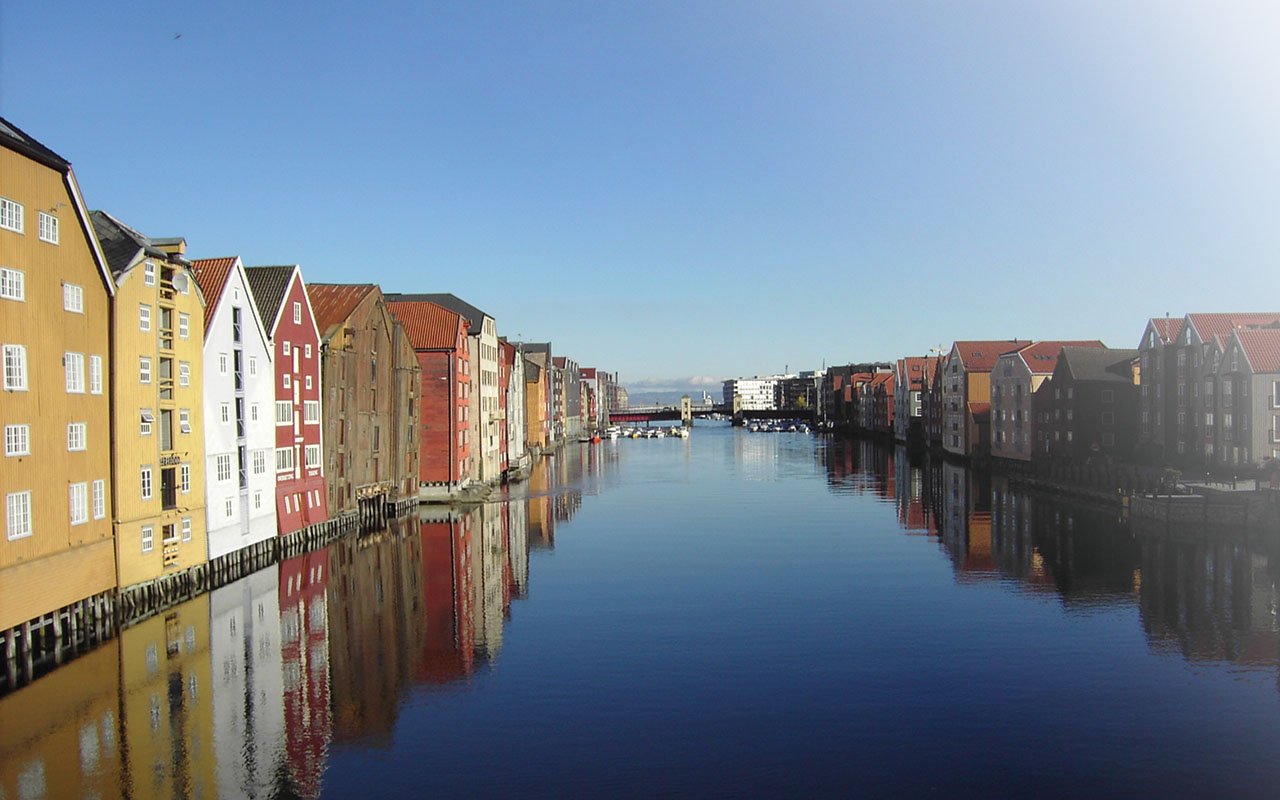 Bilde av Nidelva, med hus langs vannkanten på begge sider og en bro bak i bilde.