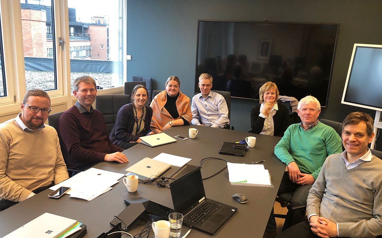 På bildet er en grupper med mennesker som sitter rundt et bord i et møterom.